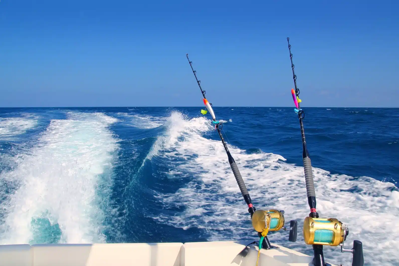 Trolling fishing boat rod and golden saltwater reels deep blue ocean sea wake 1767007874590
