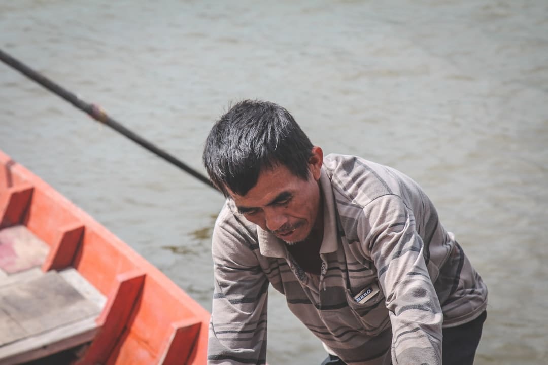 A close-up, powerful shot of a fisherman straining against the boat's rail, demonstrating the immense physical effort required to land a large offshore fish.